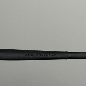 K&ouml;nnte beinhalten: Nahaufnahme eines schwarzen Brillenb&uuml;gels mit dem wei&szlig;en Aufdruck "MADE IN U.S.A.". Der B&uuml;gel besteht aus mattem Material und vor grauem Hintergrund.