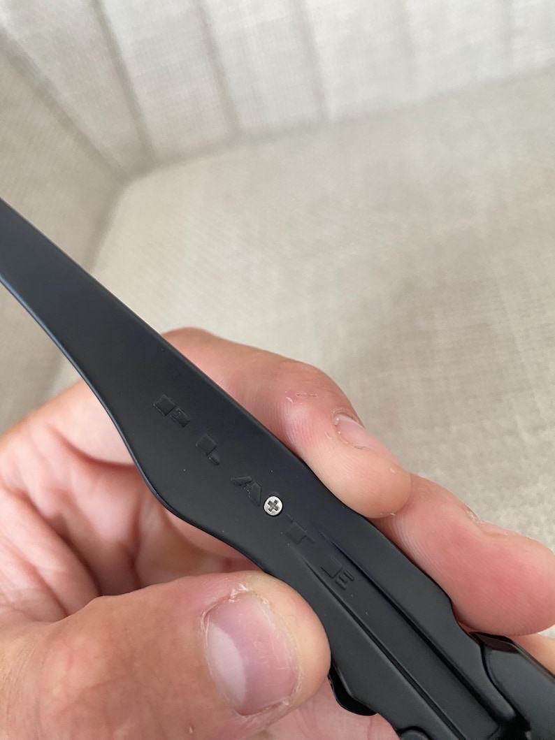 May include: Close-up of a black eyeglass arm with the brand name "POLICE" engraved. The arm is held by a hand and features a small silver screw. The glasses appear to be made of a matte black material.