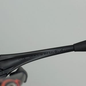 May include: Close-up of black sunglasses with the text "MADE IN U.S.A." printed on the arm. The sunglasses have a sleek, modern design with a matte finish. The frame is black, and the lenses are not visible.