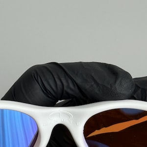 May include: White sunglasses with blue and brown lenses. The sunglasses have a white frame and the word "MINUTE" is printed on the top of the frame.