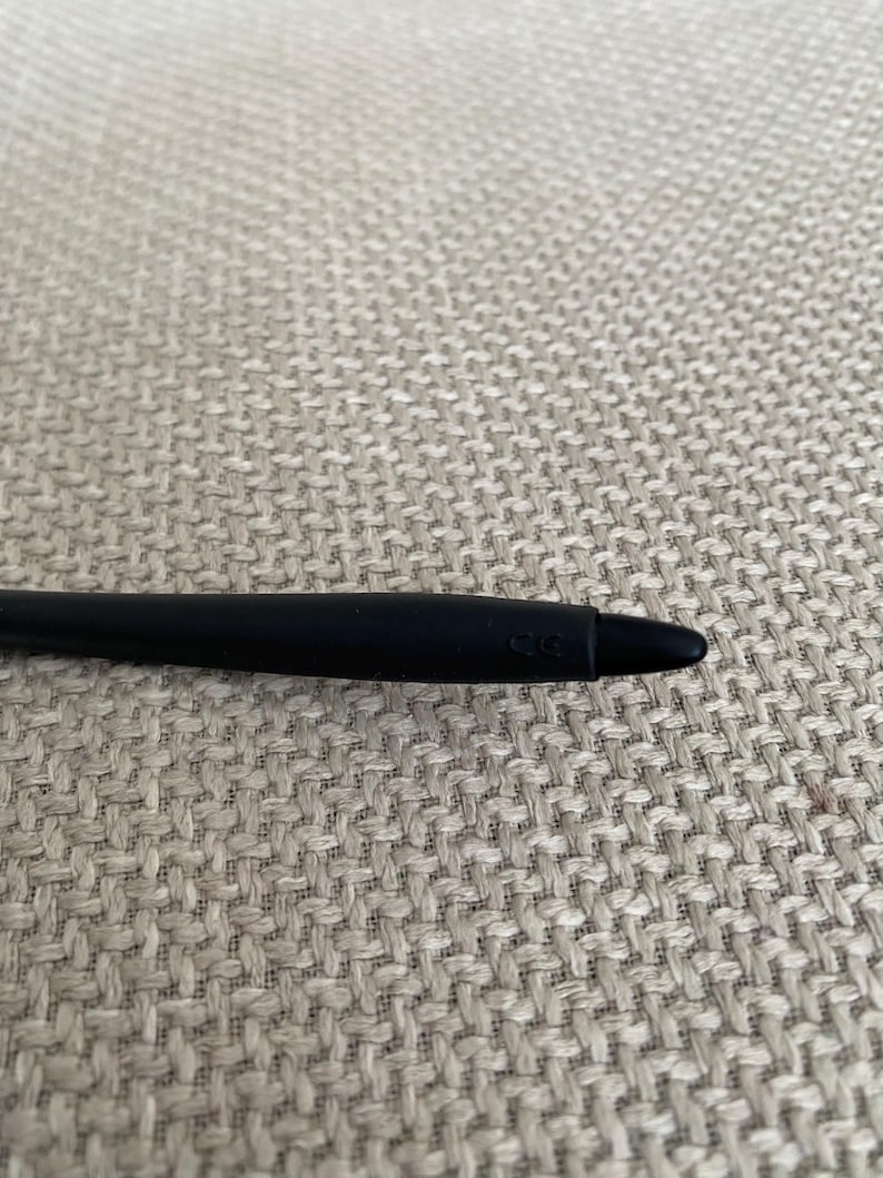 Puede incluir: Un l&aacute;piz &oacute;ptico negro con punta redondeada. El l&aacute;piz &oacute;ptico est&aacute; sobre una superficie beige texturizada. El l&aacute;piz &oacute;ptico tiene las letras "CG" impresas en el lateral.
