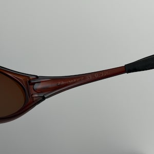 May include: Close-up of brown sunglasses with dark lenses. The frame is a dark brown color with the text "MADE IN U.S.A." printed on the arm.
