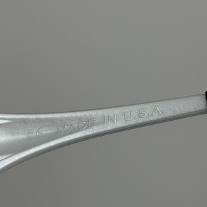 May include: A close-up shot of a silver object with the text "MADE IN U.S.A." embossed on its surface. The object has a curved, elongated shape and appears to be made of metal. The background is a solid, light grey colour.