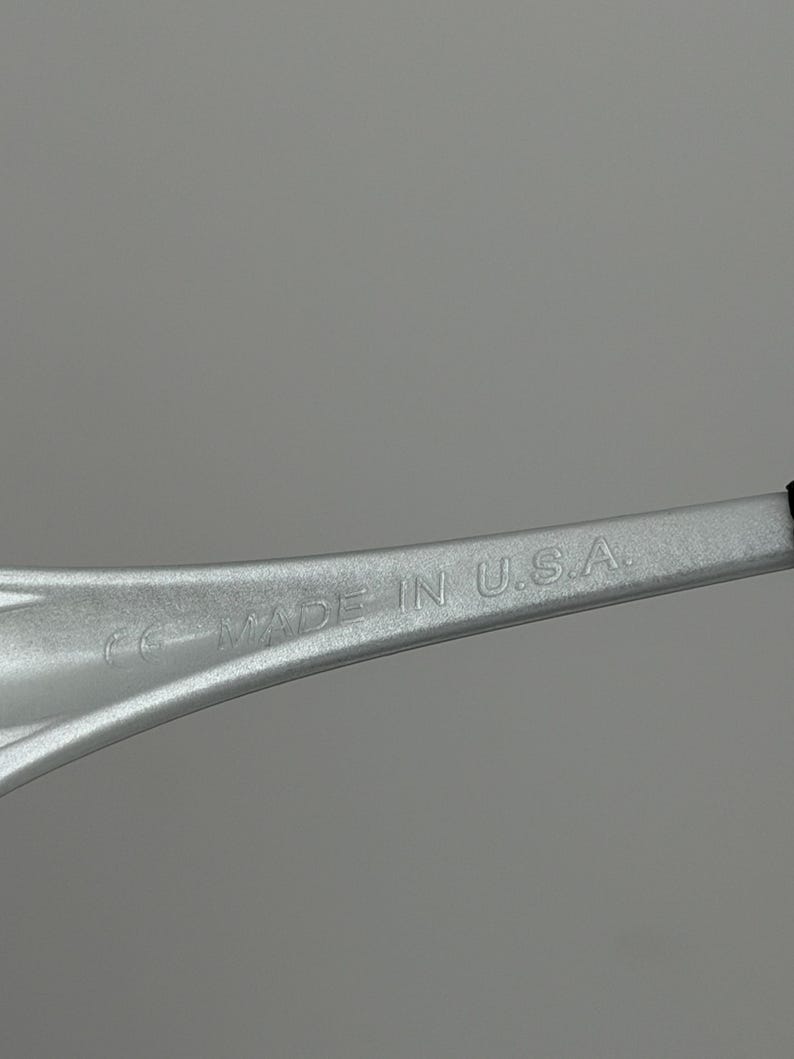 May include: A close-up shot of a silver object with the text "MADE IN U.S.A." embossed on its surface. The object has a curved, elongated shape and appears to be made of metal. The background is a solid, light grey colour.
