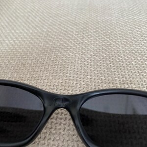 Puede incluir: Gafas de sol negras con lentes oscuras. Las gafas de sol tienen un dise&ntilde;o elegante y curvado y un acabado mate. La montura presenta un logotipo sutil en el puente. Las lentes parecen estar tintadas, ofreciendo protecci&oacute;n solar.
