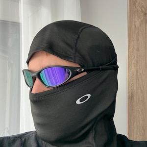 May include: Black balaclava and sunglasses. The balaclava covers the head and neck, with a small white logo on the side. The sunglasses have a black frame and reflective lenses with blue and green hues.
