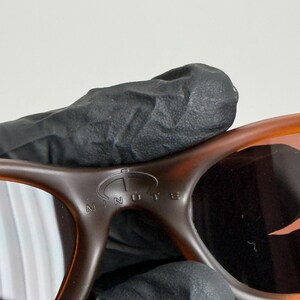 May include: Close-up of brown sunglasses with a tortoise shell pattern. The sunglasses have a curved design and the word "MINUTE" is visible on the frame. The lenses are a dark color.