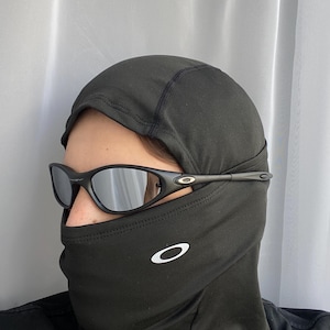 Puede incluir: Pasamonta&ntilde;as negro con un logotipo blanco y gafas de sol negras. Las gafas de sol tienen montura negra y lentes espejadas. El pasamonta&ntilde;as cubre la cabeza y el cuello.