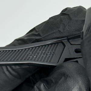 K&ouml;nnte beinhalten: Nahaufnahme eines schwarzen Teppichmessers mit dem Wort "CLIFDEN" auf dem Griff. Das Messer wird von einer behandschuhten Hand vor wei&szlig;em Hintergrund gehalten. Der Griff hat ein geriffeltes Design f&uuml;r besseren Halt.