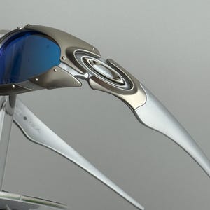 May include: Silver-framed sunglasses with blue lenses. The sunglasses have a sleek, modern design with a metallic finish. The lenses are a vibrant blue, contrasting with the silver frame. The arms of the sunglasses are long and slender.