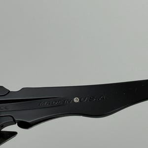 May include: Close-up of a black object with the text "MADE IN U.S.A." printed on it. The object has a sleek, modern design and appears to be made of a durable material. The background is a solid, neutral gray.