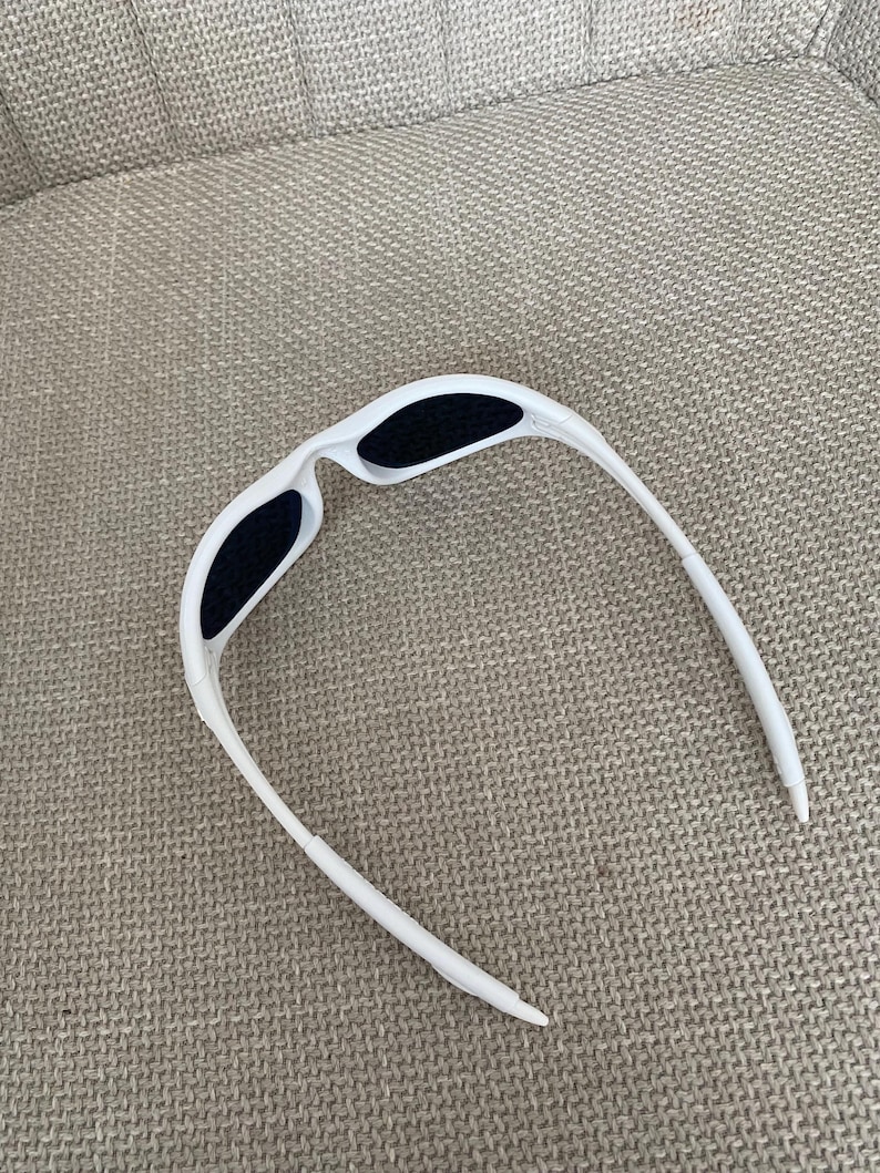 Puede incluir: Gafas de sol blancas con lentes negras. Las gafas tienen un dise&ntilde;o elegante y moderno con una montura curvada y una forma aerodin&aacute;mica. Las lentes son oscuras, proporcionando contraste con la montura blanca.
