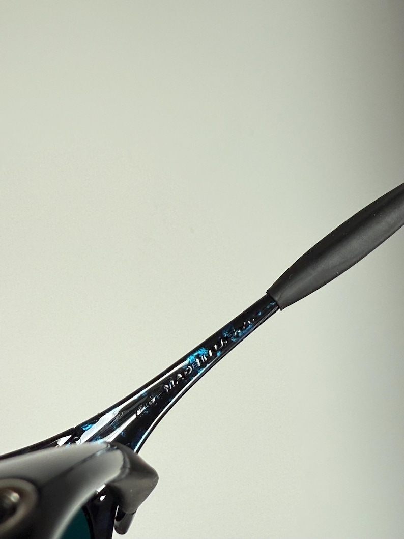 Puede incluir: Primer plano de una montura de gafas negra y azul. Las palabras "MADE IN U.S.A." son visibles en la varilla. La montura tiene un dise&ntilde;o elegante y moderno con una patilla de goma negra.