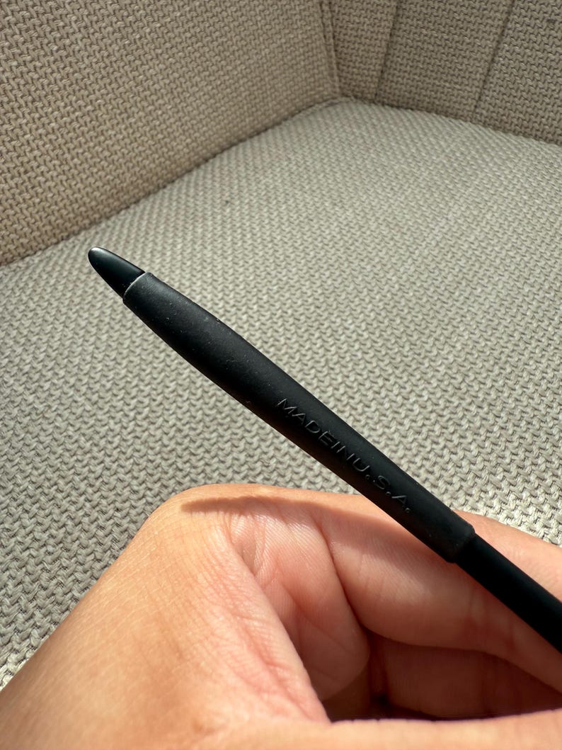 May include: A black stylus with a rounded tip. The stylus is marked with the text "MADE IN U.S.A." The stylus is held in a hand.