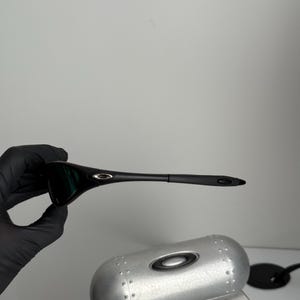 May include: Black sunglasses with a sleek, modern design. The sunglasses have dark lenses and a black frame. A silver case and a black accessory are also visible.