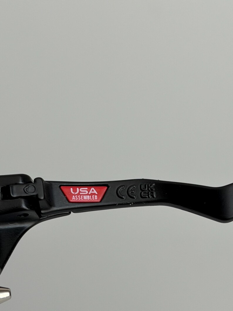 May include: Black lever with the text "USA Assembled" in a red rectangle. The lever also has the CE mark. The lever is likely a component of a bicycle or motorcycle.
