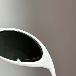 以下が含まれることがあります： 黒いレンズの白いサングラス。 サングラスは、太い白いフレームを備えた、洗練されたモダンなデザインです。 レンズは暗く、ブランド名「PRIZM」がレンズに表示されています。