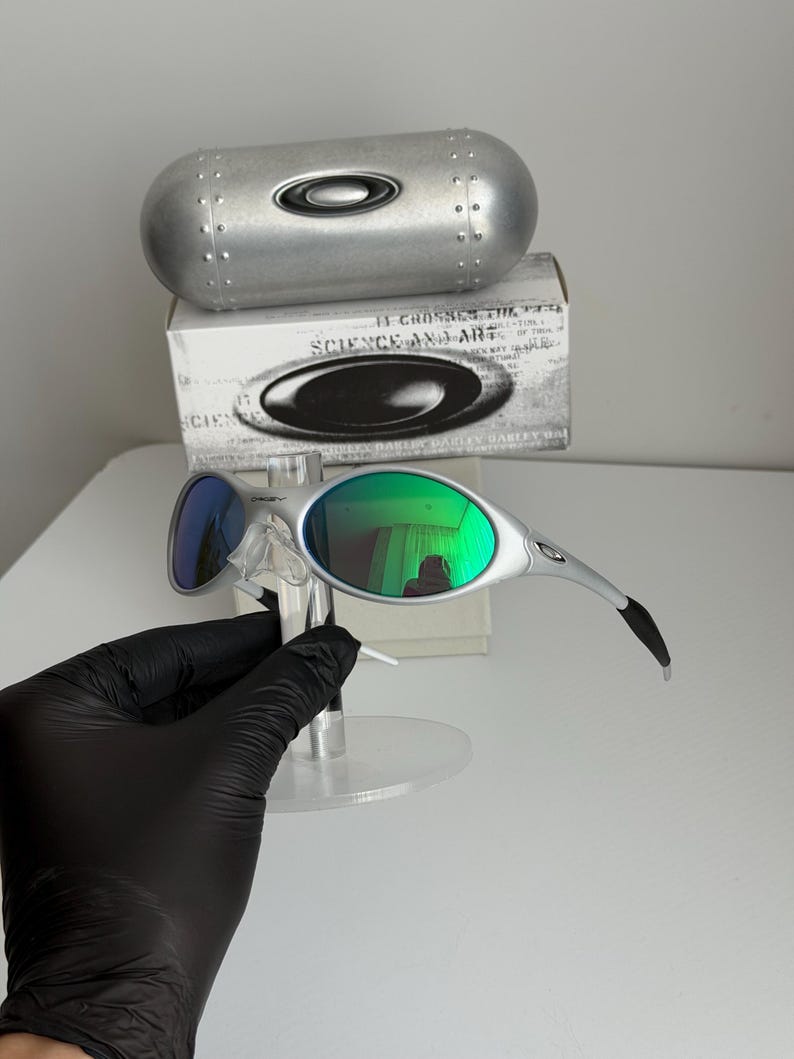 May include: Silver-framed sunglasses with green mirrored lenses and blue mirrored lenses. The sunglasses are displayed with a silver case and a box with the text "SCIENCE AND ART".