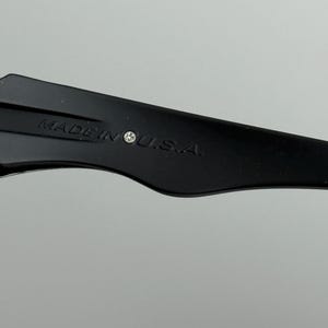 May include: Close-up of a black object with the text "MADE IN U.S.A." printed in white. The object has a curved shape and is set against a light gray background.