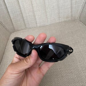 May include: Black wraparound sunglasses with dark lenses and a glossy black frame. The arms are thick and curved. The lenses are slightly tinted, offering protection from the sun.
