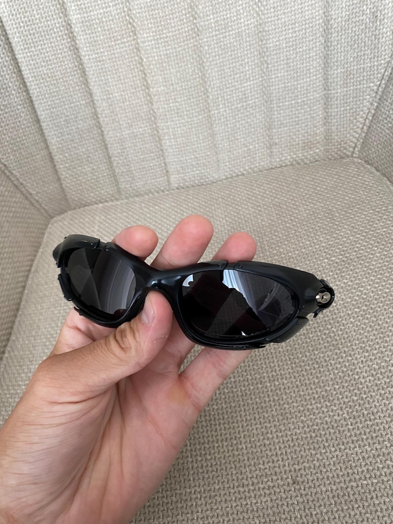 May include: Black wraparound sunglasses with dark lenses and a glossy black frame. The arms are thick and curved. The lenses are slightly tinted, offering protection from the sun.