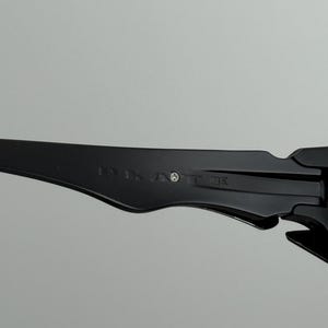 May include: Close-up of a black sunglasses arm with the text "131. AOTT DE" printed on the side. The sunglasses arm is made of a smooth, matte material.