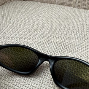 May include: Black sunglasses with dark lenses. The sunglasses have a sleek, modern design with a matte finish. The frames are thick and wrap around the lenses, providing a stylish and functional accessory.
