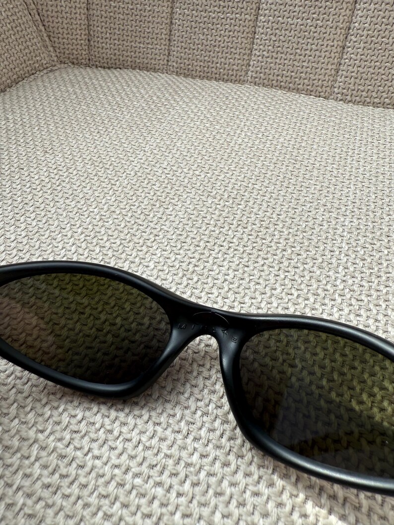 May include: Black sunglasses with dark lenses. The sunglasses have a sleek, modern design with a matte finish. The frames are thick and wrap around the lenses, providing a stylish and functional accessory.