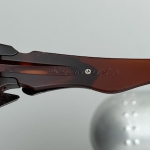 May include: Close-up of the arm of a pair of sunglasses. The arm is brown with a tortoiseshell pattern and the text "MADE IN U.S.A." is visible. A small silver screw is also visible.
