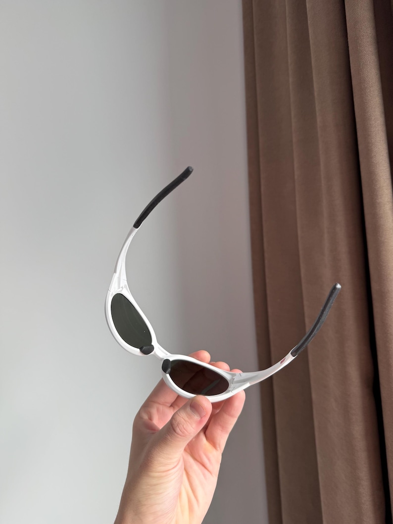 以下が含まれることがあります： 白いフレームと濃い色のレンズのサングラス。 サングラスは、テンプルに黒いアクセントが付いた、洗練されたモダンなデザインです。 フレームは軽量素材で作られているようです。