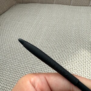 May include: A black stylus with a rounded tip. The stylus is marked with the text "MADE IN U.S.A." The stylus is held against a textured, neutral-toned background.