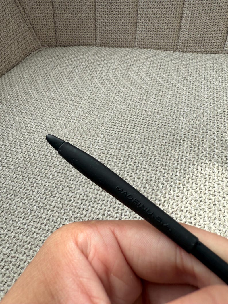May include: A black stylus with a rounded tip. The stylus is marked with the text "MADE IN U.S.A." The stylus is held against a textured, neutral-toned background.
