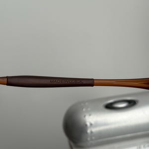 May include: Close-up of brown eyeglasses with the text "MADE IN U.S.A." on the temple. The frame is a light brown color, and the temple has a darker brown grip.