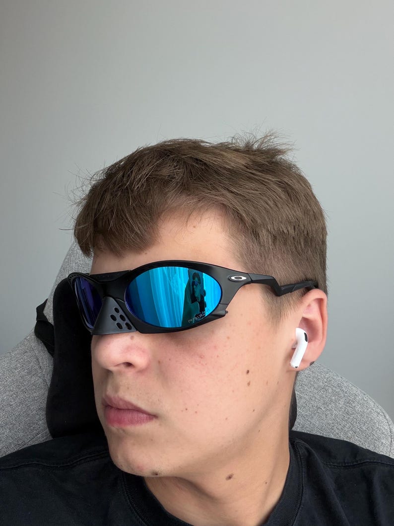 May include: Black sports sunglasses with blue mirrored lenses. The sunglasses have a distinctive design with a nose bridge and a sleek, modern frame. The lenses reflect a blue hue, and the frame is black.