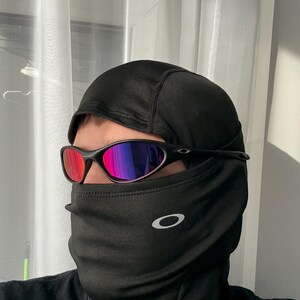 May include: Black balaclava with a white Oakley logo and black sunglasses with red and purple lenses. The sunglasses have a black frame. The balaclava covers the head and neck.