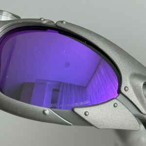 May include: Close-up of gray sunglasses with purple polarized lenses. The lenses reflect the surrounding environment. The frame has a riveted design. The word "POLARIZED" is printed on the lens.