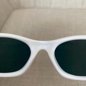 Puede incluir: Gafas 3D blancas con lentes oscuras. Las gafas tienen un dise&ntilde;o curvo y la palabra "MINUTE" est&aacute; impresa en el puente. Las gafas est&aacute;n hechas de un material liso y brillante.