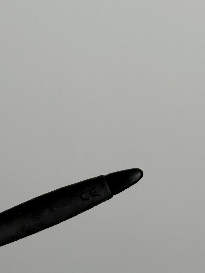 May include: A black stylus with a rounded tip. The stylus has a matte finish and a curved design. The letters "CE" are printed on the side of the stylus.