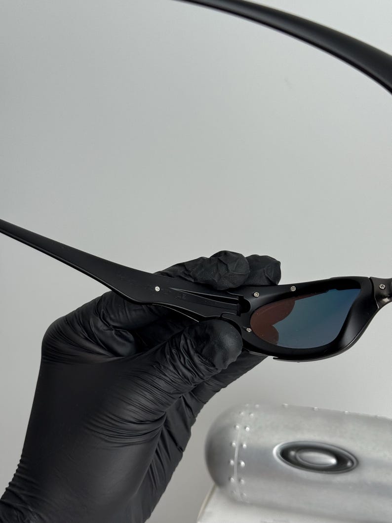 May include: Black sunglasses with a sleek, modern design. The lenses have a gradient effect, transitioning from a dark color to a lighter hue. The frames are matte black, and the arms are thin and angular.