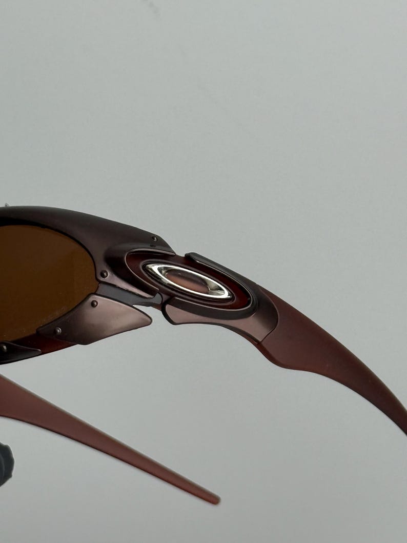May include: Close-up of brown sunglasses with a metallic frame. The sunglasses have a curved design with a silver accent near the hinge and brown tinted lenses. The arms of the sunglasses are a darker brown.