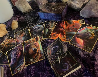 May include: A deck of Cosmic Animalia oracle cards with a gold and black box. The cards feature colorful illustrations of animals with intricate details. The box has the title "Cosmic Animalia" on the front.