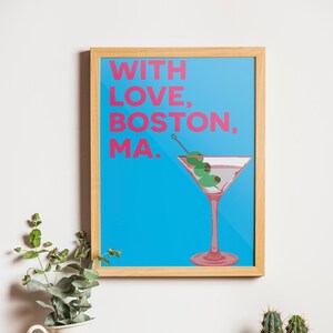 May include: A framed print with a blue background and the text "WITH LOVE, BOSTON, MA." in pink. A martini glass with olives is in the bottom right corner of the print.