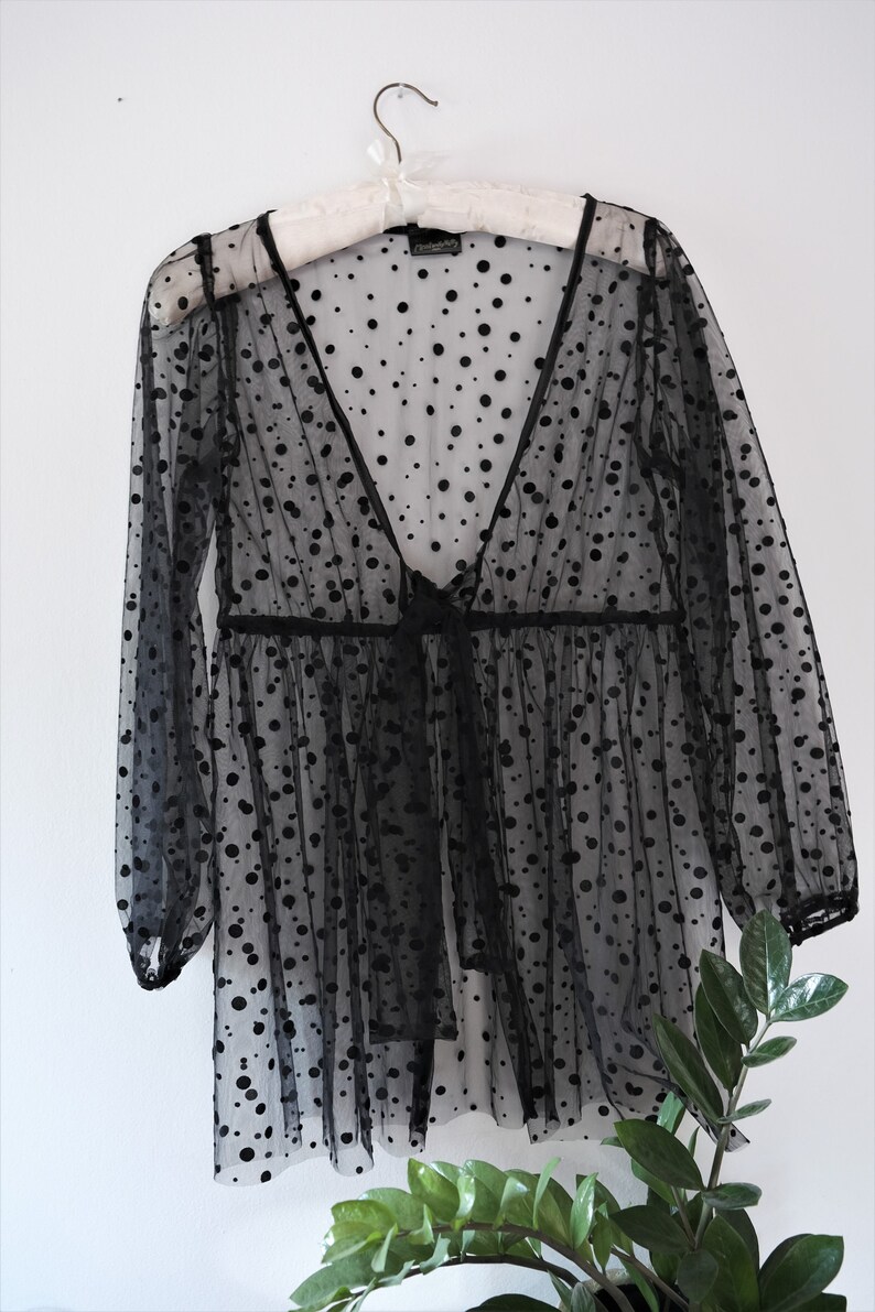 May include: Black sheer polka dot top with long sleeves and a V-neck. The top has a tie at the waist.