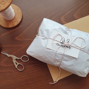 May include: A white gift bag tied with a pink ribbon and a small white tag with the text "Miss Funk Natty" on it.