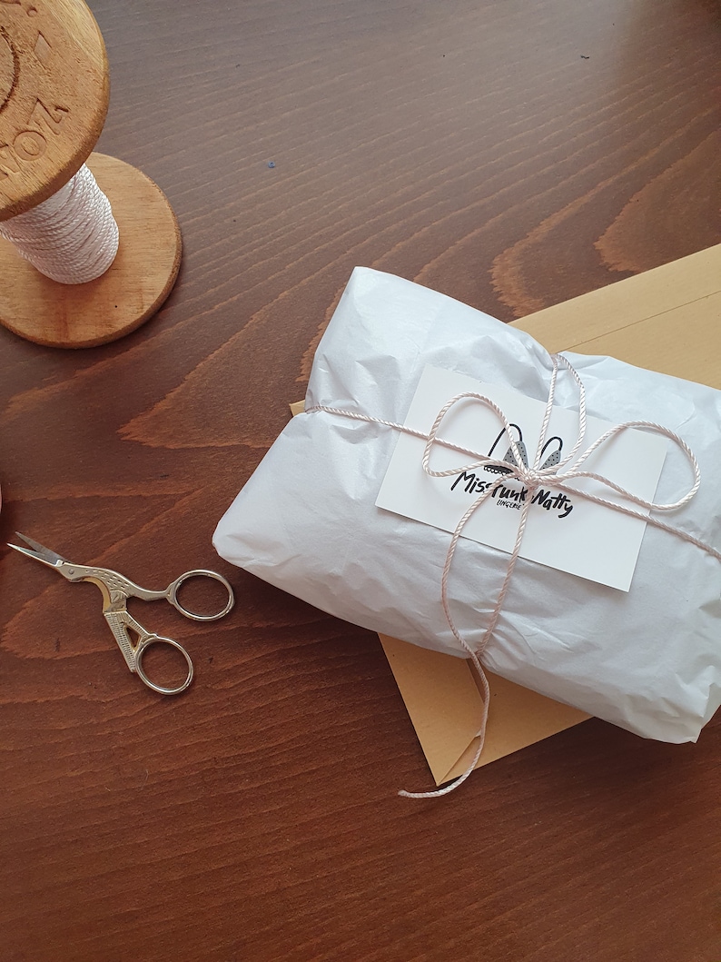 May include: A white gift bag tied with a pink ribbon and a small white tag with the text "Miss Funk Natty" on it.