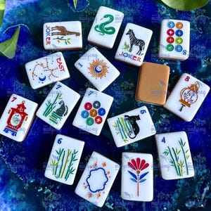 May include: A collection of white Mahjong tiles with various illustrations and numbers. The tiles feature images of a zebra, snake, and a giraffe. Some tiles have the word "Joker" and numbers.