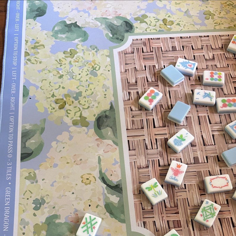 May include: A board game with a floral design and a woven texture. The game includes rectangular tiles with various colorful illustrations and blue tiles. The text on the board reads "RIGHT-OVER-LEFT | OPTION TO STOP LEFT-OVER-RIGHT | OPTION TO PASS 0-3 TILES GREEN DRAGON."