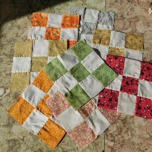 May include: A collection of colorful patchwork squares in various stages of completion. The squares feature a checkerboard pattern with white squares alternating with orange, green, yellow, red, and floral fabrics. These are likely quilt blocks.