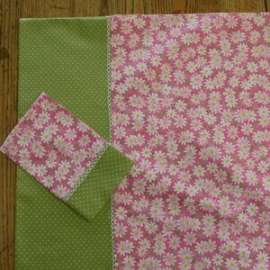Peut inclure: Un tissu vert à pois blancs et un tissu rose à fleurs blanches. Le tissu rose est bordé d'une dentelle blanche.