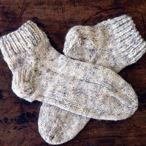 Puede incluir: Un par de calcetines de punto en un patrón moteado beige y marrón. Los calcetines están doblados y tienen un diseño de punto de cable en la parte superior.